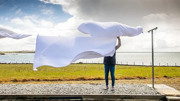 On a blustry day a woman brings in the sheets from the line, before the onset of heavy showers outside Kinsale.   (Photo: David Creedon)