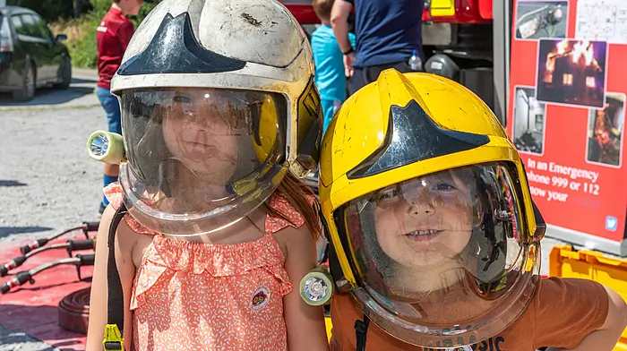 Schull, West Cork, Ireland. 28th Jul, 2024. The sun shone for Schull Agricultural Show today. Hundreds of people attended to watch many horse classes. Trying on firefighter's helmets for size were Saoirse & Fionn Hayes from Schull. Picture: Andy Gibson.