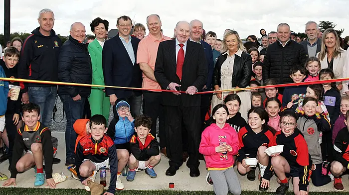 Newcestown GAA club president Seán Crowley surrounded by his club officers, invited guests and the future generation of players, cutting the tape to officially open the new Astroturf sports complex and second pitch, Páirc Uí Mhathúna,  last Saturday evening.   (Photo: Paddy Feen)