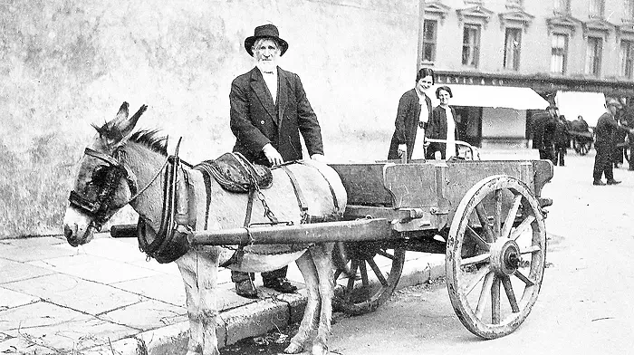 Man with donkey and cart at standing at the top of Market Street, Skibbereen, with the Square in the background, c1920s.
