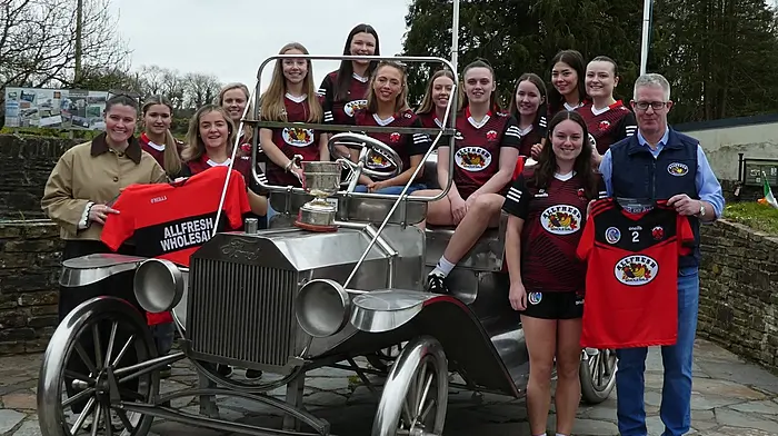 Adult camogie players posing at the iconic Model T in Ballinascarthy with their new Allfresh Wholesale jerseys. From left: Holly Sweetnam, Nicole Prochniak, Megan Ryan, Kate O'Donovan, Ciara Hayes, Sarah Cahalane, Orlaith Dee, Ella Cahalane, Sinéad McCarthy, Michelle O'Driscoll, Katelyn O'Neill, Anna Cullinane, Clara Crowley and Barra Sweetnam.