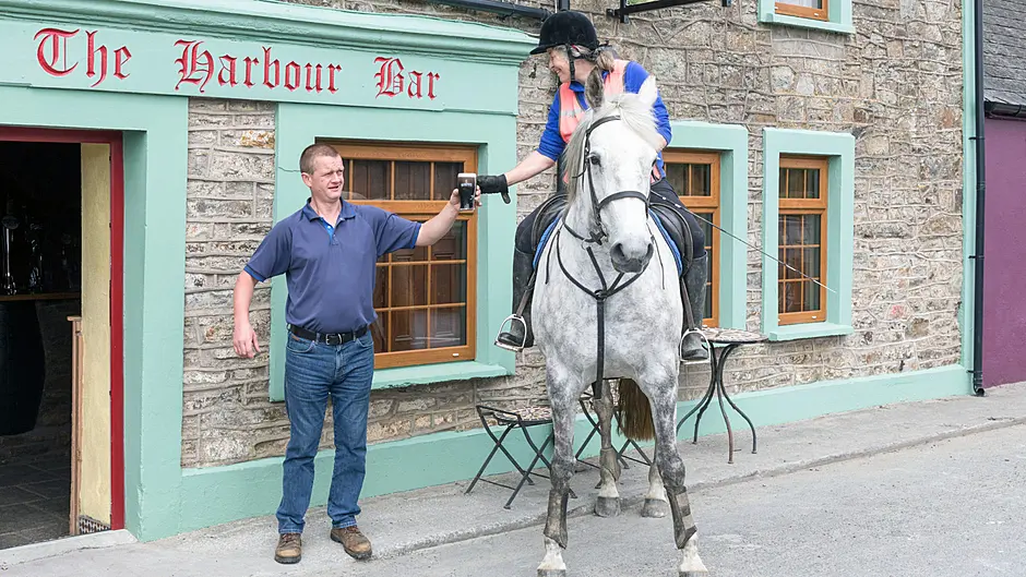 Publican Frank Walsh serves a pint of creamy stout to his first customer in six months, Imogen Bertin and her horse 
Hatbox when they called to the Harbour Bar in Robert’s Cove. (Photo: David Creedon / Anzenberger)